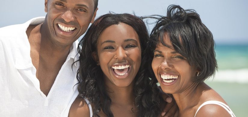 A happy smiling laughing African American family of father mother & daughter at the beach in the summer